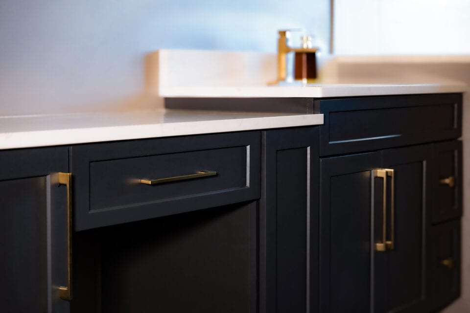 A modern kitchen with dark cabinets and gold handles features a sleek quartz countertop, enhancing the contrast with the cabinetry. A soap dispenser is visible in the background, adding a touch of elegance.