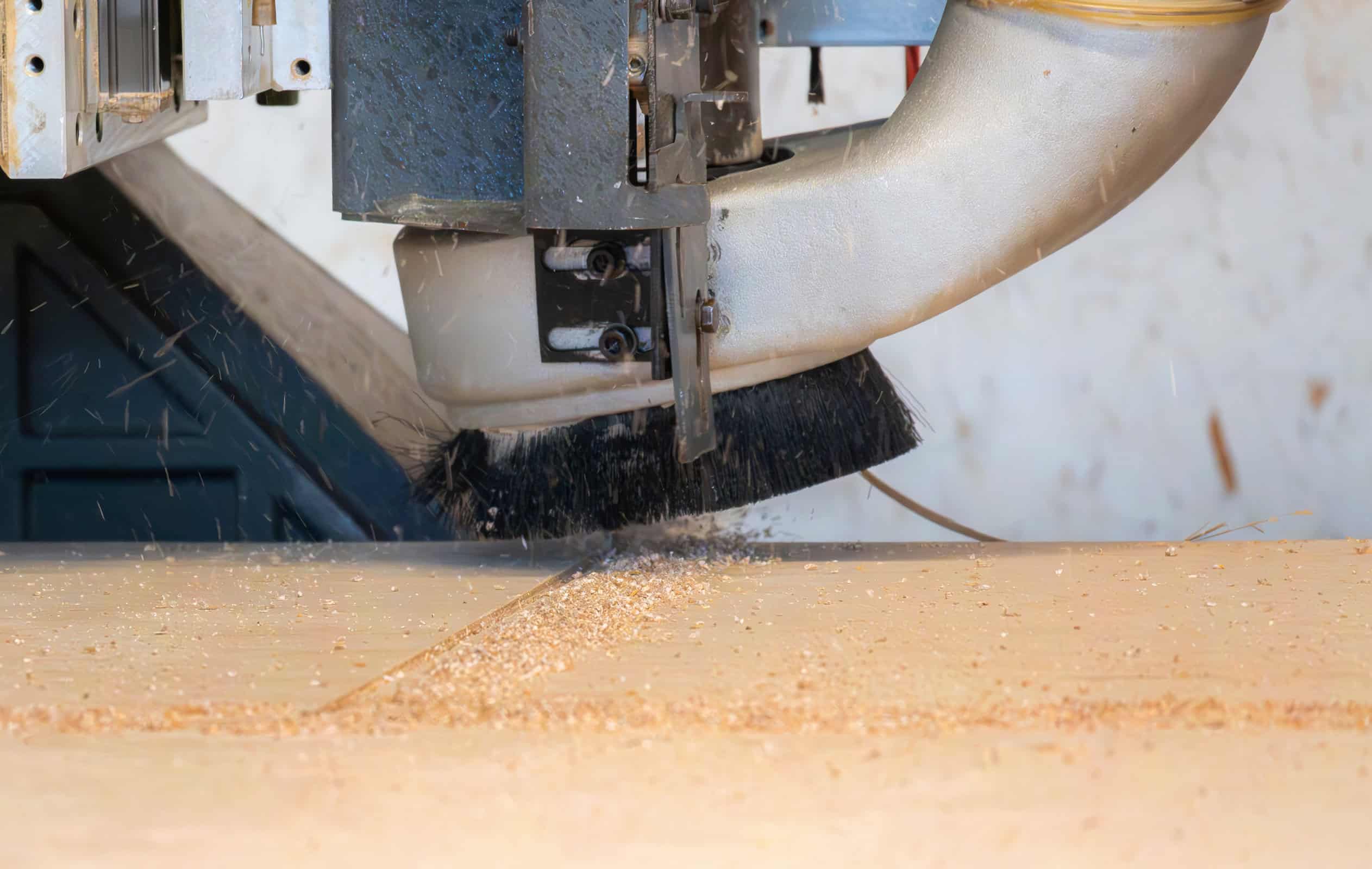 A close-up of a CNC machine cutting a piece of wood, with wood shavings scattering as it operates. The brush and metal components are visible beside the securely mounted wood, evoking the precision and artistry akin to crafting a natural stone countertop.