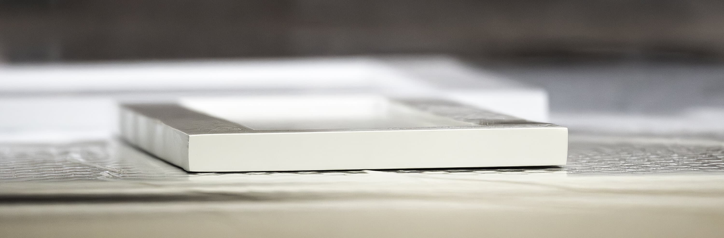 Close-up of a rectangular white object resting on a natural stone countertop. The object is raised slightly at the base, casting a delicate shadow underneath. The blurred background enhances the focus on the foreground, creating an elegant and timeless scene from Knoxville's finest kitchens.